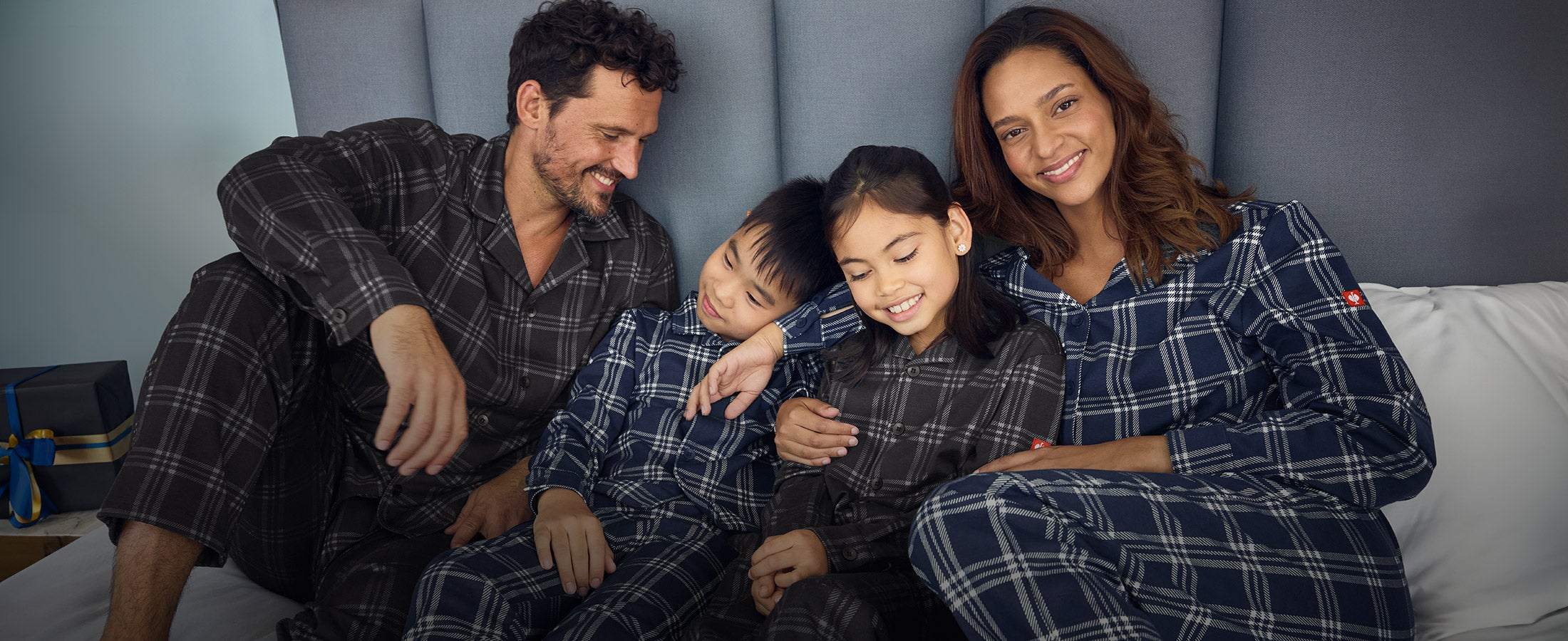 Vrouw, man, meisje en jongen dragen e.s. ruitjes-pyjama's op een bed